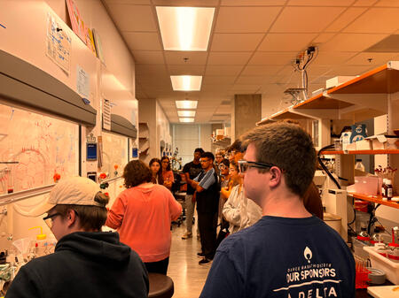 Undergraduate students look on as a graduate student gives a tour of an organic chemistry research lab