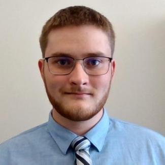 Head shot of Stephen Goodlett, man with glasses and short brown hair, wearing a blue shirt