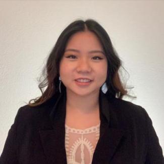 Head shot of Ngan H Thai, Asian woman with long dark hair, wearing a black jacket and lace blouse