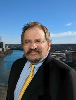 Head shot of bearded man with glasses; river and partial skyline in the background