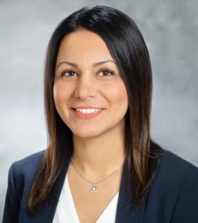 Headshot of speaker; female with dark hair and eyes, wearing white shirt and navy blue jacket