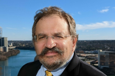 Head shot of bearded man with glasses; river and partial skyline in the background